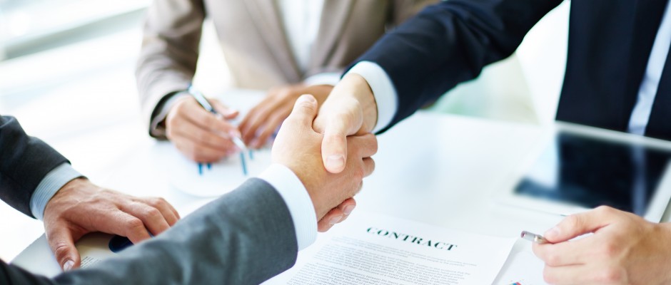 Image of business partners handshaking over business objects on workplace
